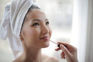 Woman with a towel on her head smiling as lip gloss is applied to her lips