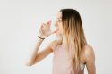 Woman sipping water, showcasing a healthy lifestyle against a light background.