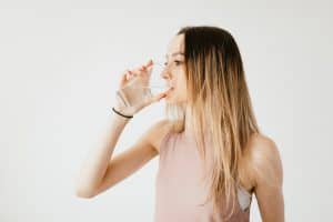 Woman sipping water, showcasing a healthy lifestyle against a light background.