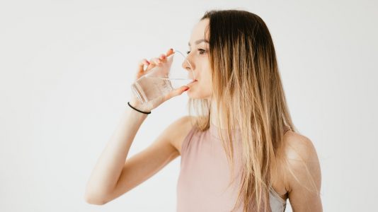 Woman sipping water, showcasing a healthy lifestyle against a light background.